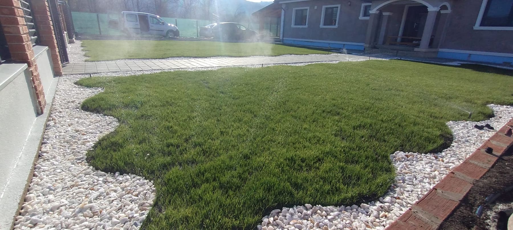 Gazon cu contur organic, încadrat de piatră decorativă, cu aspersoare în funcțiune
